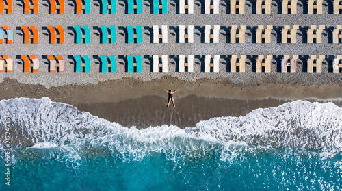 Aerial view of woman lying on pebble beach with colorful loungers