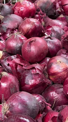 Purple red onions piled in wooden crates and cardboard boxes create a colorful market display, offering fresh vegetables for shoppers, grocery stores and local produce sales. Close up.