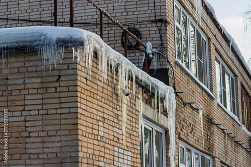 Obraz na plátně Sharp icicles hang dangerously from the edge of a brick building roof under a la