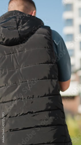 Close up of man walking away from camera on outdoor path wearing black puffer vest over blue shirt and checkered flannel. focus remains steadily on his back as man moves forward
