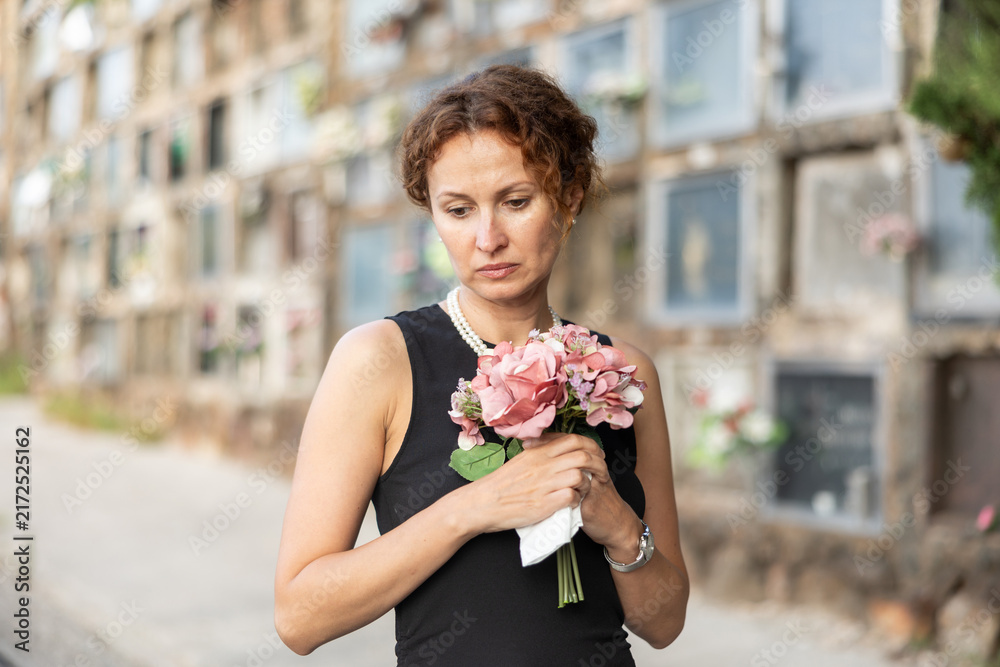 Fototapeta premium Visit to cemetery, woman in mourning clothes grieves for deceased relative. Near grave widow grieves and prays for soul of deceased relative, moment of remembrance, to pay tribute to memory