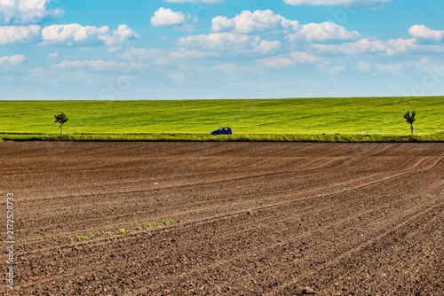 Plowed farmland with green fields and a car on a country road