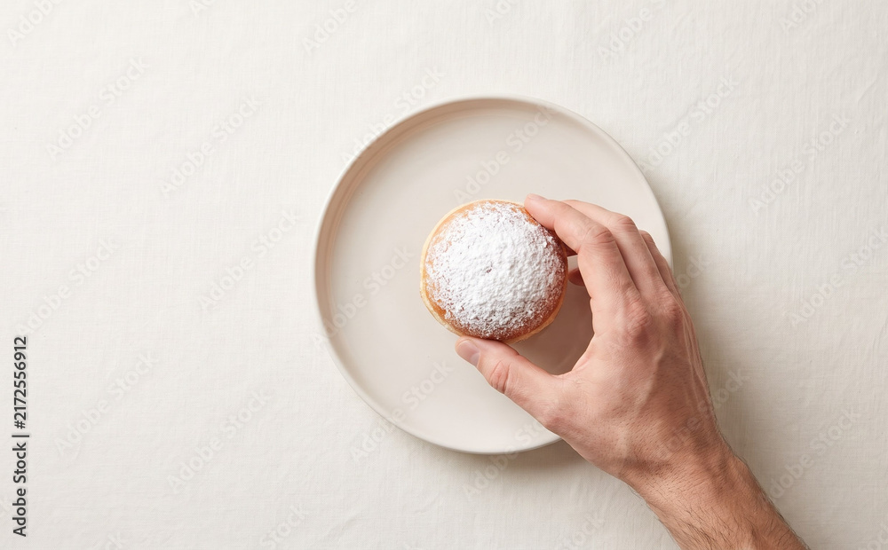 Obraz premium Hand holding a sweet powdered donut on a white plate representing delicious bakery and dessert concepts