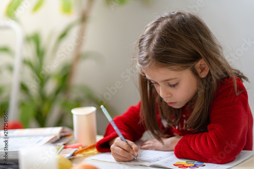 Fotografía Young girl concentrating on homework while writing in a notebook at a table with school supplies in a bright home environment