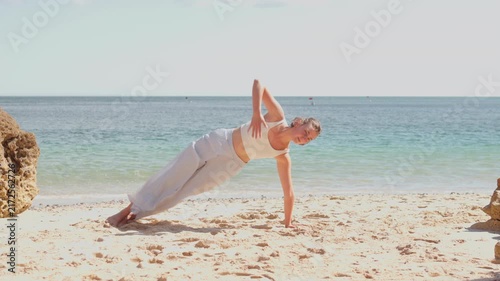 Young woman performing a plank pose on a sandy beach during an outdoor yoga workout. Core strength, fitness, and endurance concept.