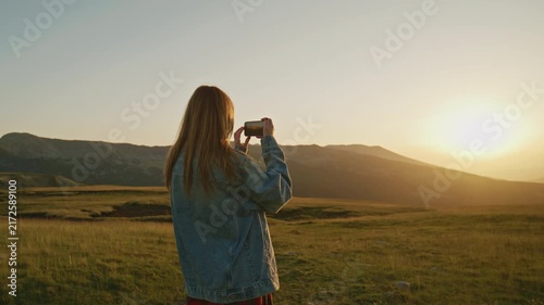 Person takes a picture of sunset in a field with mountains in the background during evening time