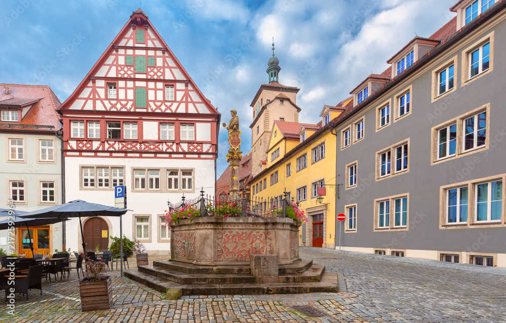 Fototapeta premium Traditional half-timbered buildings and an ornate stone fountain on a cobblestone square in Rothenburg ob der Tauber, Germany.