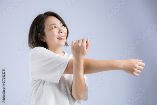 [Blue Background] A woman in her 40s smiling as she stretches to stay healthy during menopause; fitness exercises to loosen up before working out