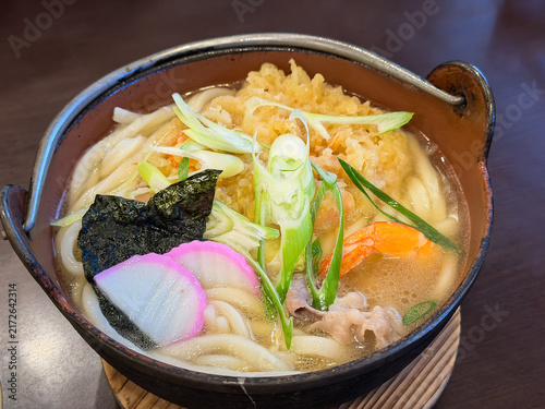 Fototapeta 日本の冬によく食べられる鍋焼きうどん。かき揚げ風の海老天とネギと蒲鉾をトッピング。