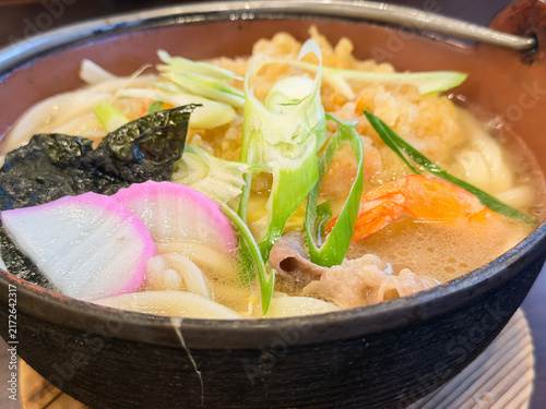 Fototapeta 日本の冬によく食べられる鍋焼きうどん。かき揚げ風の海老天とネギと蒲鉾をトッピング。クローズアップ。