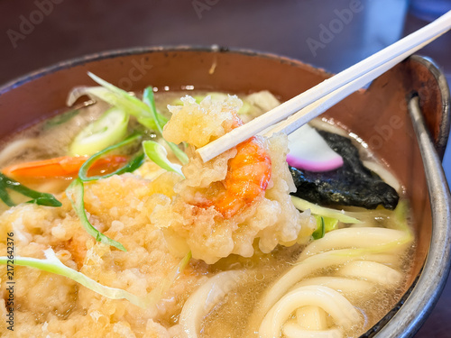 Fototapeta 日本の冬によく食べられる鍋焼きうどん。えび天を箸で持ち上げている。