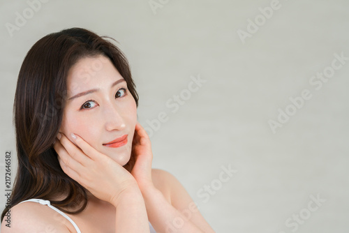 Fotografie A middle-aged Asian woman with her hand on her cheek, skincare image