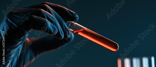 Close-up of gloved hand holding test tube with red liquid for science experiment or medical research in dark background