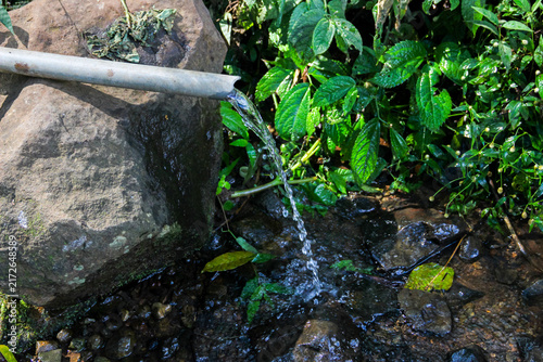 Natural spring water flowing from a pipe into a rocky stream