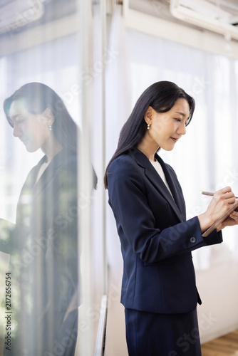 Young Japanese businesswoman taking notes on a clipboard by a bright window