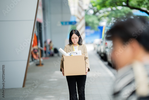 Obraz na płótnie A businessman who has lost his job walks out of the office carrying a box of his belongings, feeling sad and frustrated