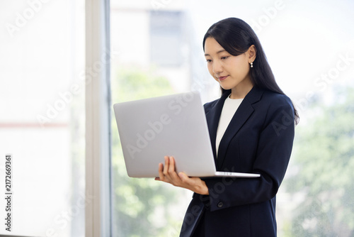 Young Japanese businesswoman working on a laptop by a bright window
