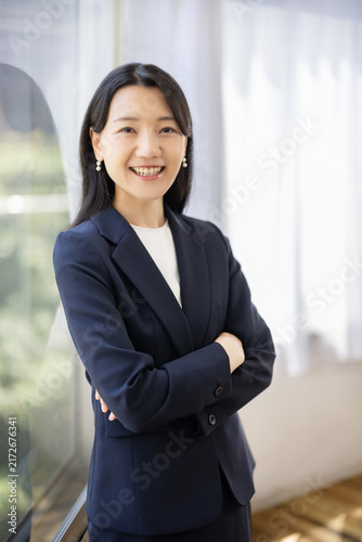 Young Japanese businesswoman standing with arms crossed and smiling at the camera by a bright window