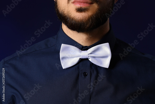 Handsome man with white bow tie on dark blue background, closeup