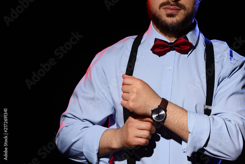 Handsome man with bow tie and wristwatch on dark background