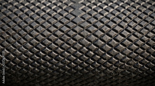 Close-up of a black, cylindrical tool handle featuring a repeating diamond-shaped knurled pattern, providing a rugged, non-slip grip texture for industrial equipment or hand tools