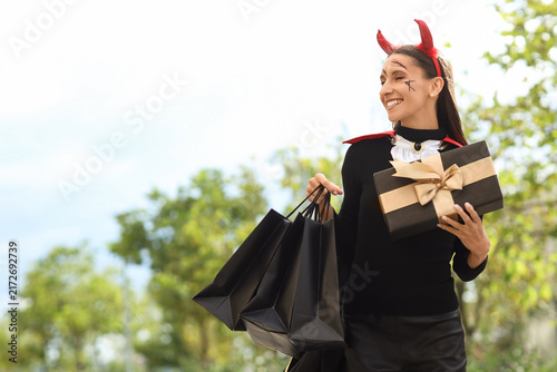 Beautiful young happy woman dressed as devil for Halloween with shopping bags...