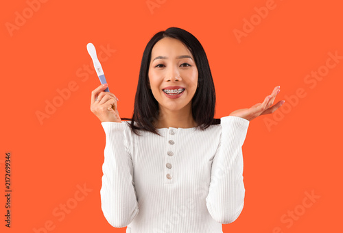 Young Asian woman with pregnancy test on orange background