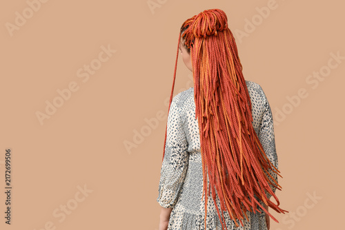 Young woman with dreadlocks on beige background, back view