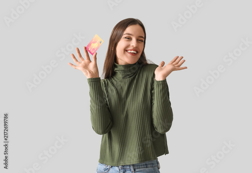 Happy young woman with credit card on light background