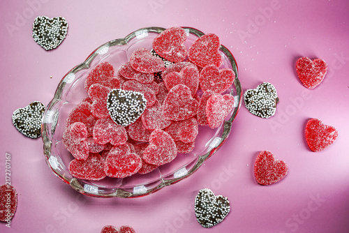 Принти на полотні Red sugar-coated heart-shaped candies and chocolate hearts with white sprinkles arranged in a glass bowl on a pink background, creating a festive Valentine's Day theme