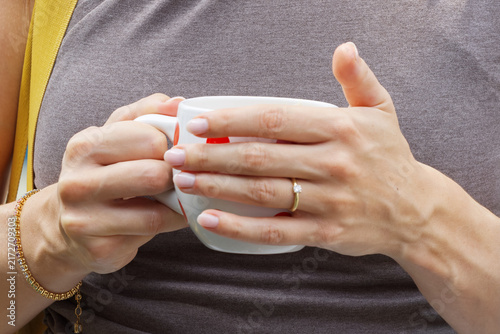 Close-up of a woman gently cradling a warm ceramic coffee mug, her engagement ring and gold bracelet catching soft light during a relaxed pause at the Naplavka market in Prague.
