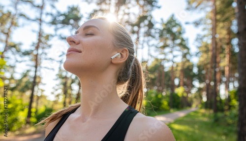 Young woman jogging in forest with wireless earbuds enjoying outdoor fitness and nature workout