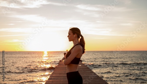 Woman jogging on wooden pier at golden sunset over calm ocean waters for fitness lifestyle