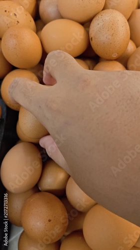 Vertical Video of Hand gently picks one egg from a pile of eggs. Fresh brown eggs fill the frame. Natural lighting highlights their smooth, rounded surfaces. The scene suggests abundance and freshness