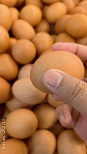 Vertical Video of Hand gently picks one egg from a pile of eggs. Fresh brown eggs fill the frame. Natural lighting highlights their smooth, rounded surfaces. The scene suggests abundance and freshness