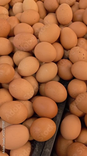 Video of Brown eggs fill the frame densely. They rest in a pile, uniform in size and hue. Some show minor blemishes, natural to their form. The surface gleams subtly under ambient light. 4K Footage