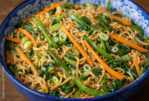 Vibrant bowl of stir fried noodles with fresh green vegetables and carrots in a blue bowl