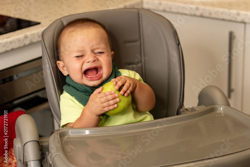 Fotografie Crying Baby Boy Holds Green Apple At Mealtime