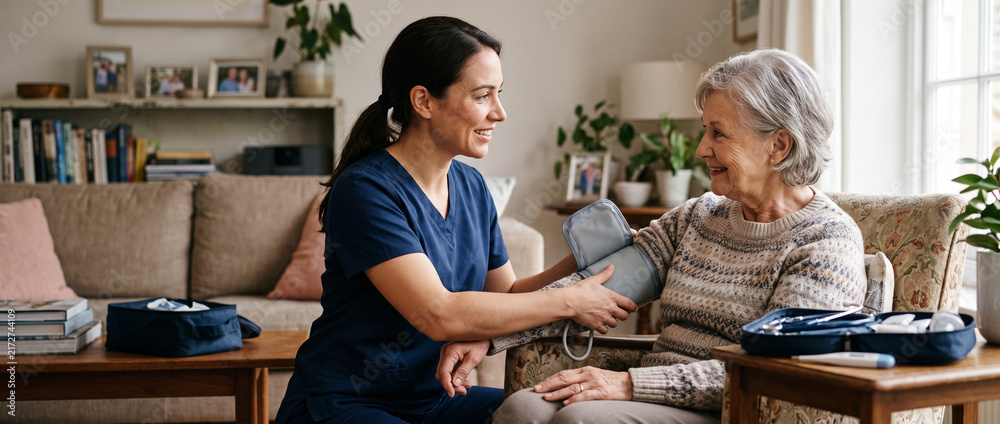 Obraz premium Home healthcare nurse checks older adult patient’s blood pressure during scheduled visit, supporting senior care, preventive monitoring, chronic care, patient safety and personalized nursing.