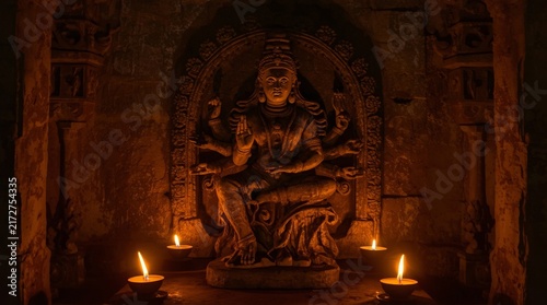 Ancient stone carved goddess statue in dark temple chamber illuminated by warm candles with captures intricately carved stone statue seated goddess within dimly lit