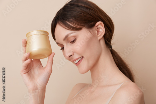 Konstfotografi Vibrant portrait of a smiling woman holding a gold cosmetic jar, highlighting a