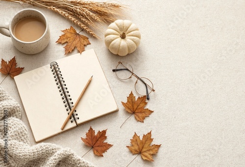 Autumnal flat lay with coffee notebook glasses and fall leaves on a textured surface