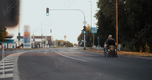 Rear view of a senior man in an electric wheelchair waiting at a red traffic light at a city intersection, showing independent urban mobility and everyday life.