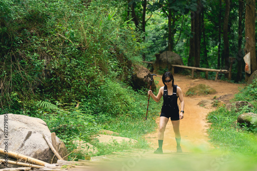 Fotografie Young woman hiking in dense green forest with walking stick exploring nature tra