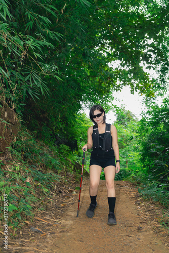 Fotografie Woman hiking trail wearing black outfit using walking stick surrounded by green
