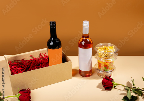 Open cardboard gift box with wine bottles and red shredded paper next to roses. Luxury wine subscription or romantic gift box concept.