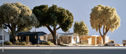 Miniature home model beneath mature tree canopy beside quiet suburban street, creating warm architectural scene with sunlight, garden planting, and residential shelter