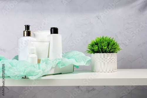 White cosmetic bottles and dispensers arranged with green fabric and a plant on a white shelf. Spa and skincare product box presentation.