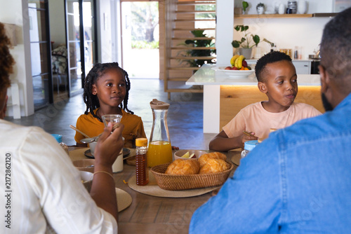 African American family eating breakfast at wooden dining table with croissant basket and juice