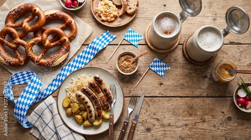 Top-down view of a traditional food spread with grilled sausages, pretzels, and ceramic beer steins on a rustic wooden table.